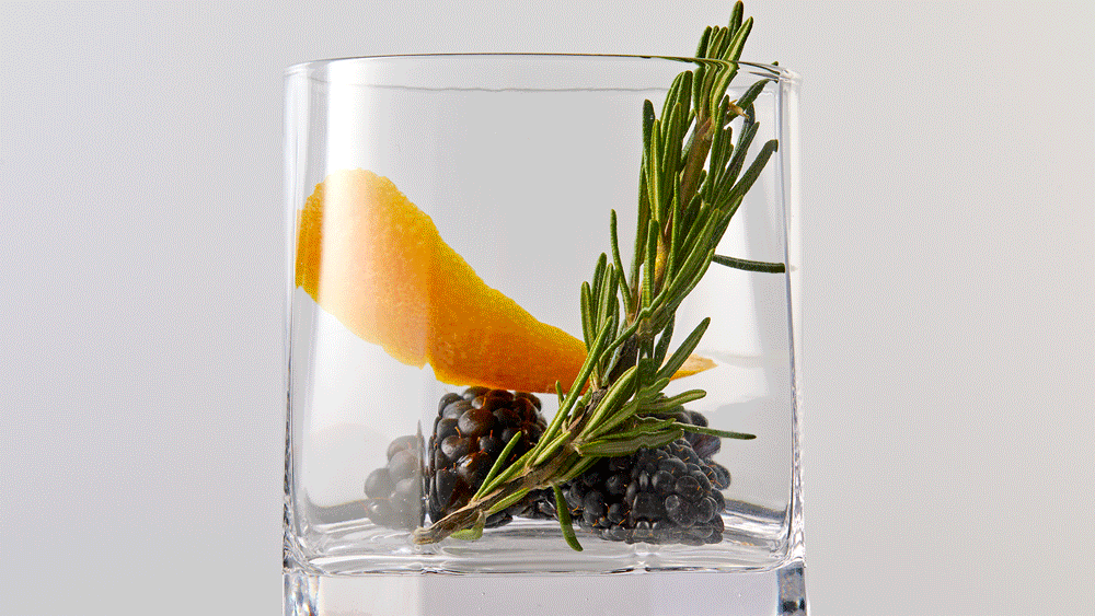 Moving .gif of a glass containing blackberries, an orange peel, and rosemary rotating and slowing filling with liquid.